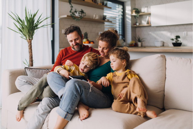 A husband and wife sit on the couch with their two children.