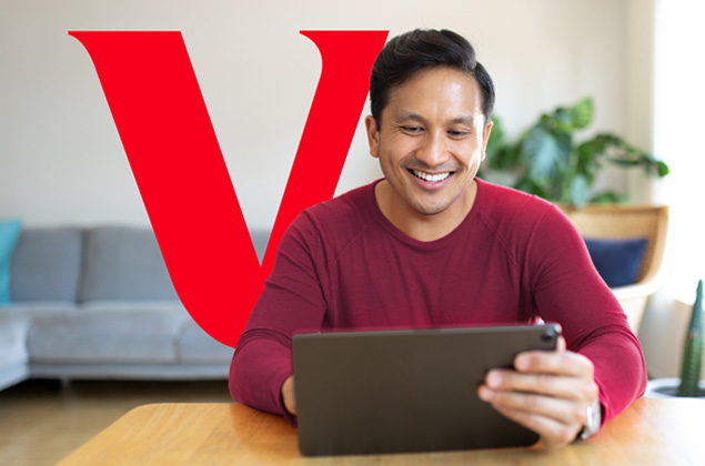 A man holding a clipboard sits in his living room while talking to an advisor on a tablet. 