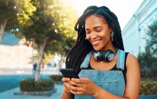 A smiling woman in a city looks at her phone.