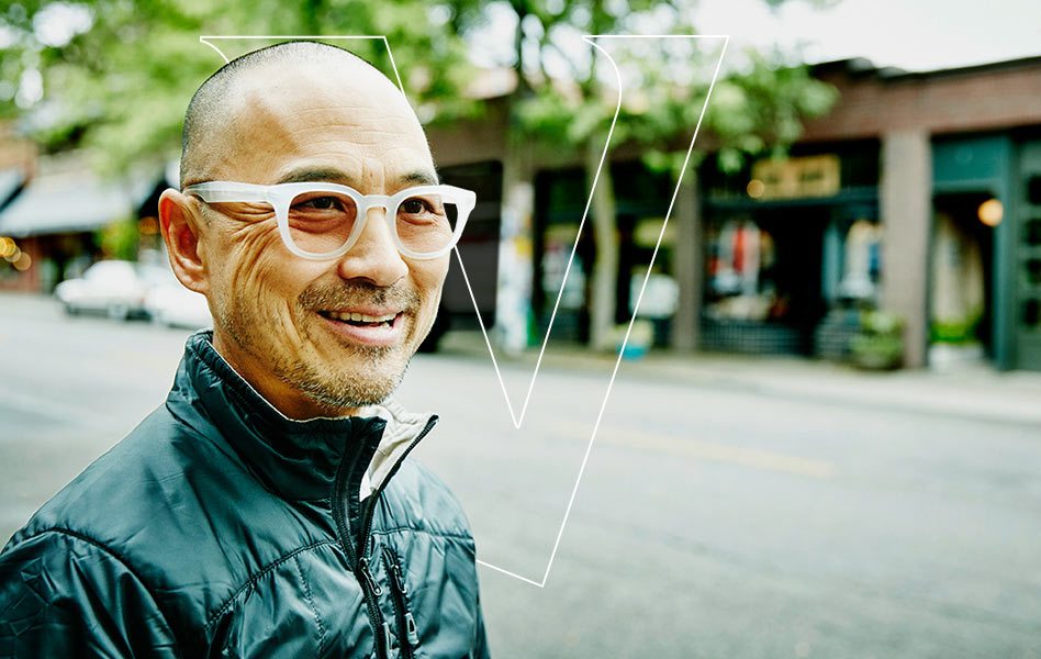 A middle-aged man walking across the street with a smile on his face and a transparent letter V behind him. 