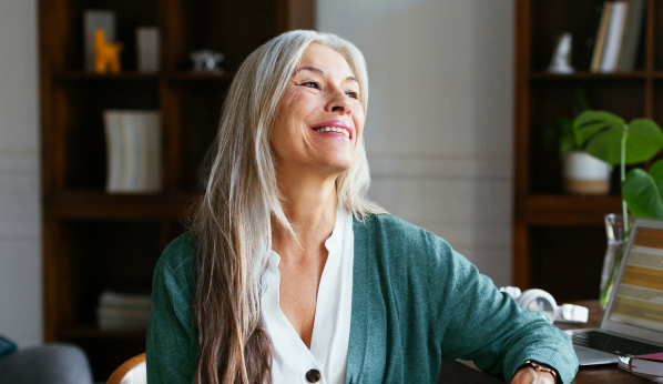 Woman with long white hair sitting by a window and smiling.