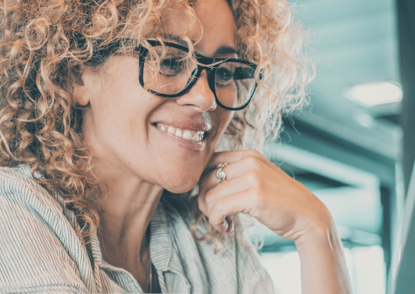   Woman with curly brown hair and black-rimmed glasses sitting at a desk and smiling.