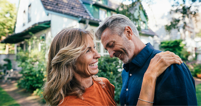 A couple smiles as they embrace in front of a house.
