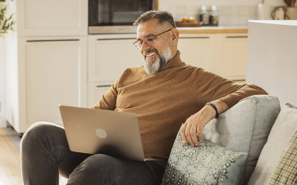 Man sitting on a couch looks at a laptop and smiles.