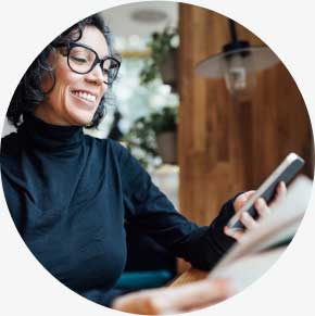 Female business professional using phone while reading a newspaper in coffee shop.