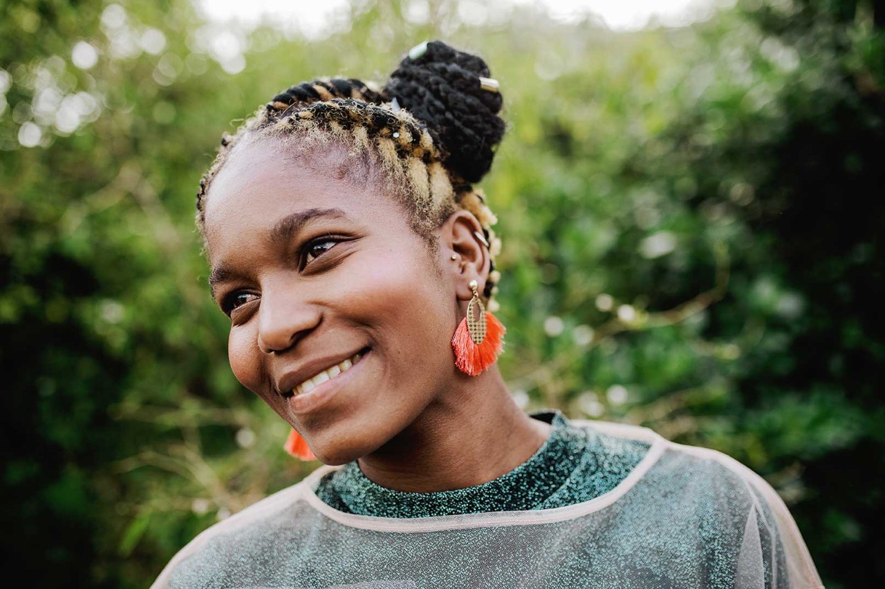 A smiling woman, with blonde and black braided hair and wearing a green top.