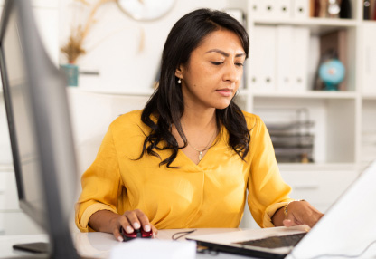 A woman is researching investment products on her laptop at a desk.
