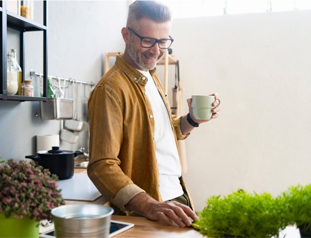 Man smiling holding a cup looking at a device