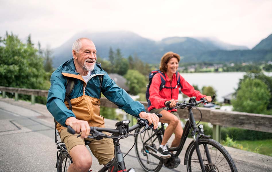 An older couple is on a bicycle ride near a large lake.