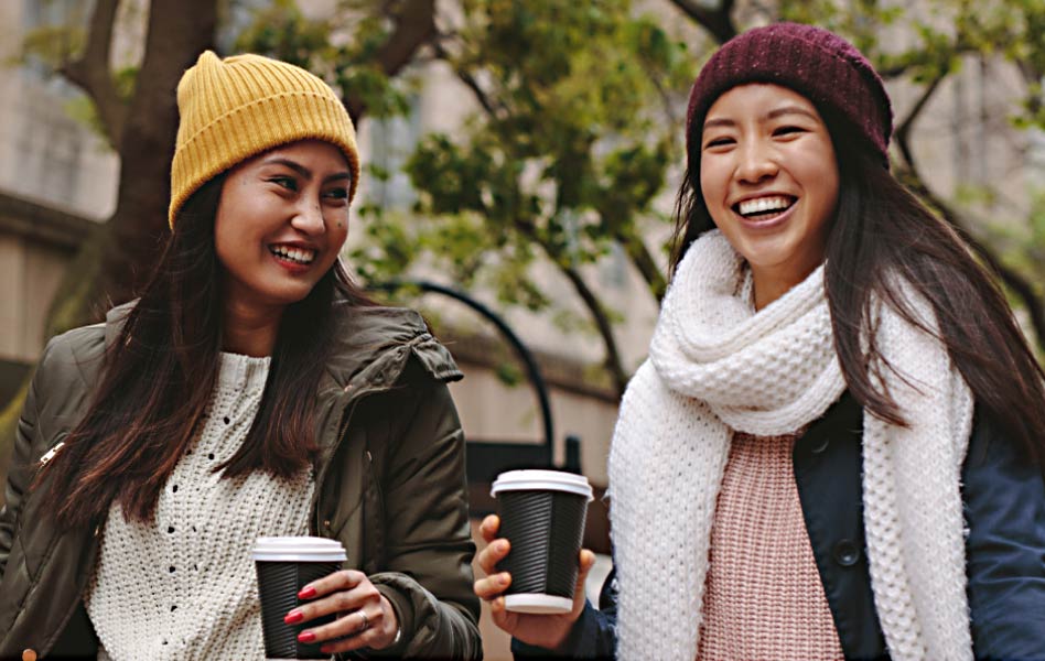 A young woman in a hat and scarf is accompanied by a smiling woman.