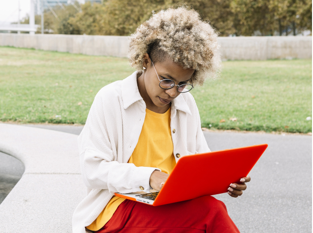  A young woman is working on a laptop outside.