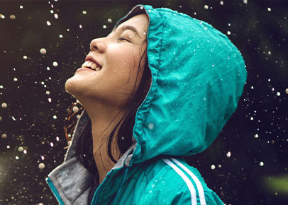 A young woman is smiling in the rain with her eyes closed.