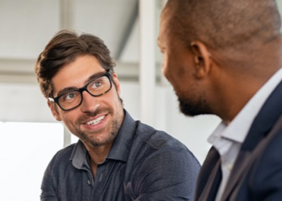 A man wearing glasses is speaking to another man just out of the frame.