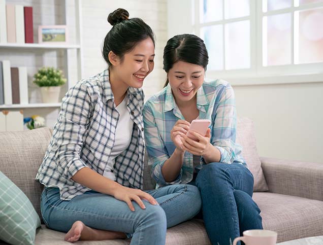 In a living room, a daughter and her mother are researching money market funds on a shared smartphone.