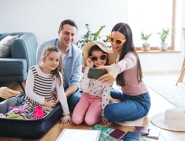 A mother is taking a selfie of herself sitting with her smiling family in the living room.