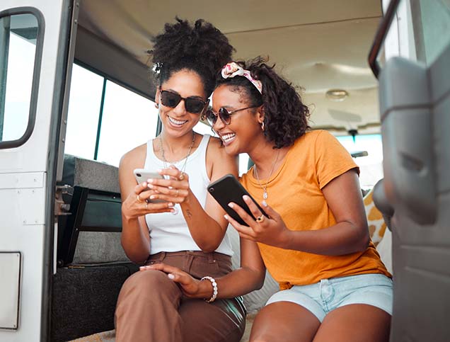 A young woman is showing her smartphone to her friend sitting next to her.