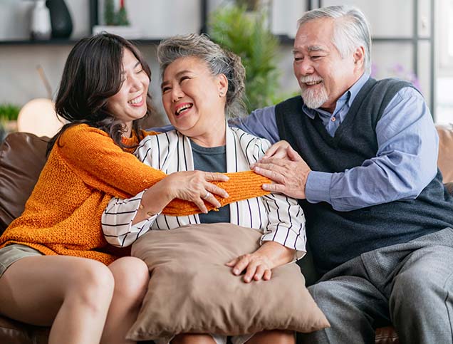 A young woman is embracing her smiling grandmother while her grandfather embraces her grandmother from the other side.