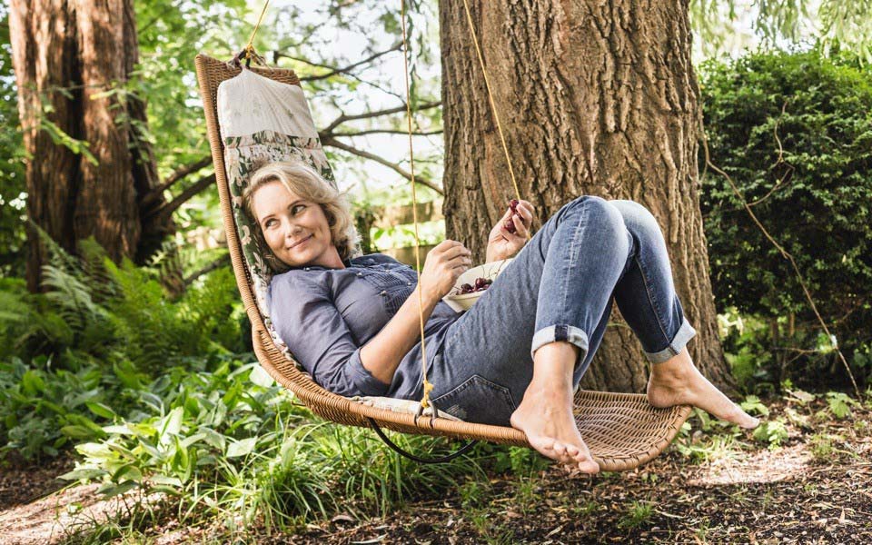 A woman is laying in a chair swing outside with a bowl of cherries in her lap