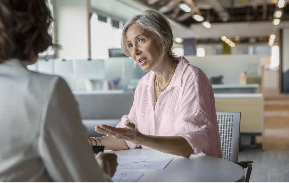 An older woman is sitting at a table having a discussion with another person just outside of the frame.