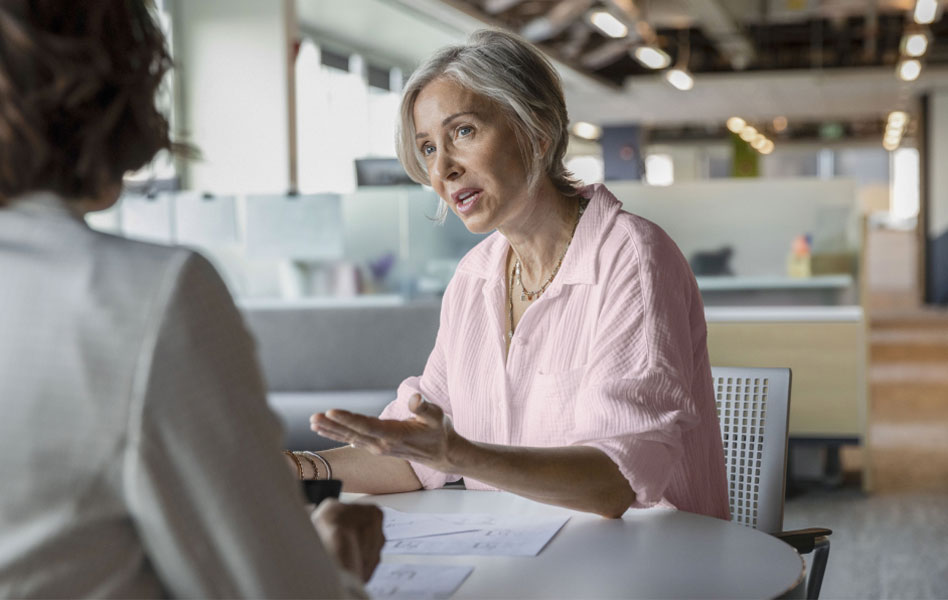 An older woman is sitting at a table having a discussion with another person just outside of the frame.