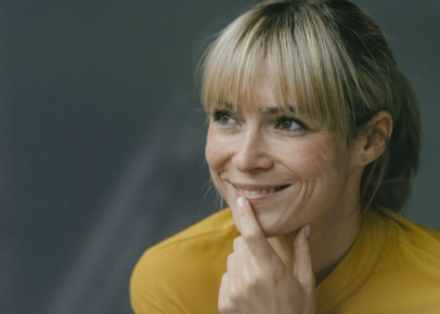 A woman is smiling while resting her chin on her hand.