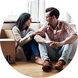 A couple surrounded by moving boxes sits in front of a window.