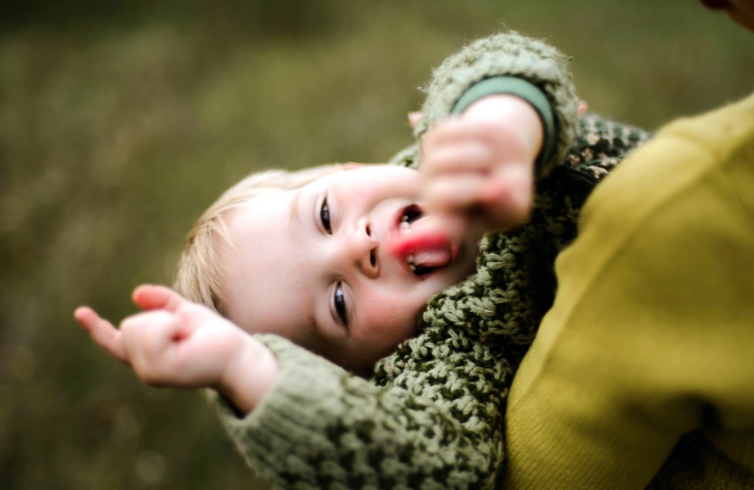 A baby is smiling and pointing at the camera.