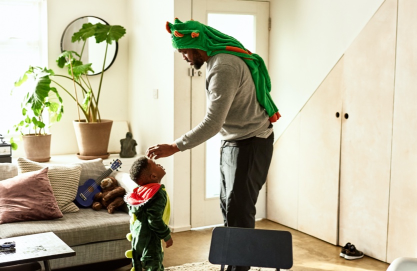 A father is touching his son’s head, both wearing dragon costumes.