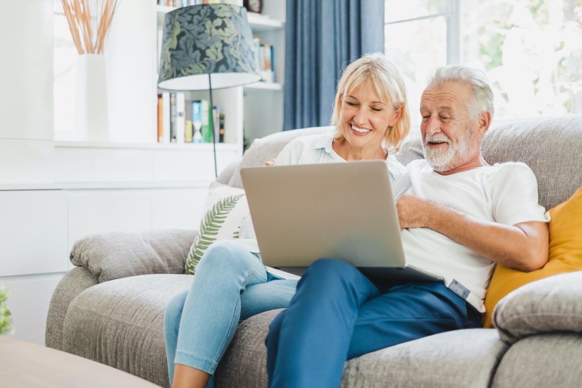 Smiling older couple sitting on a couch and looking at their laptop.