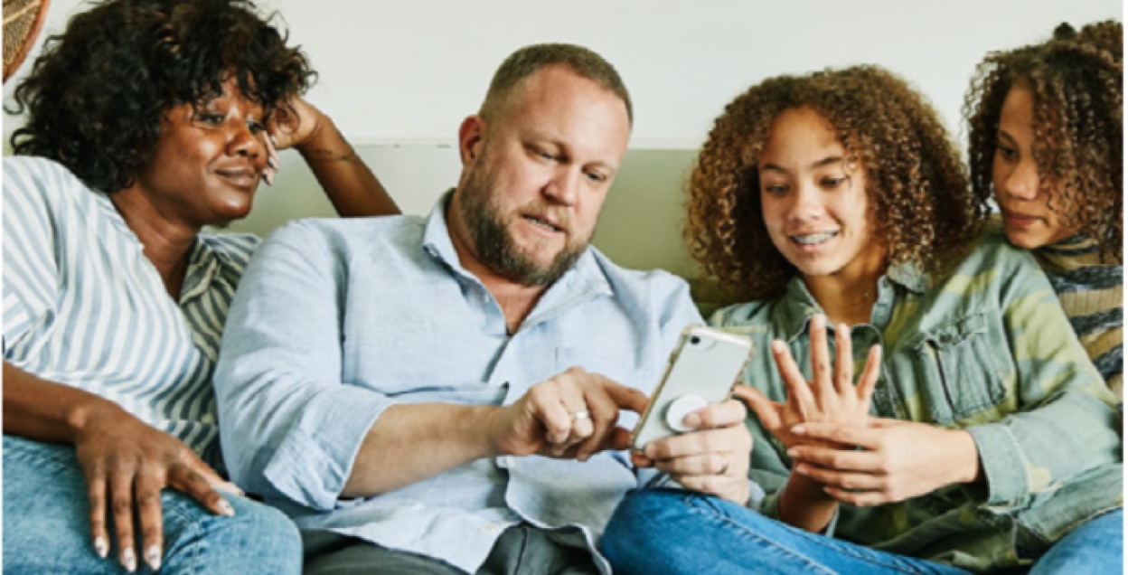 Family of four gathers around looking at the dad's phone.