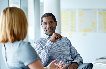 Male and female co-worker chatting while seated in an office meeting room.