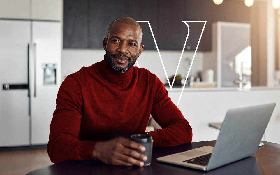 Person in a red sweater sitting at a kitchen counter with a laptop and a coffee cup.