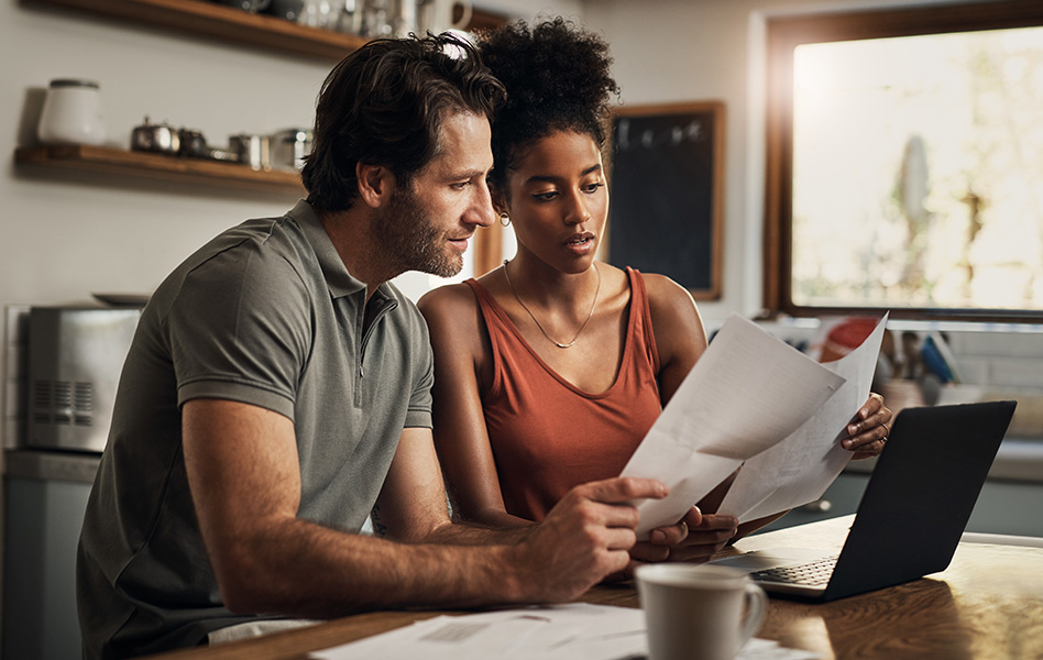 A couple sitting at their kitchen table reviews paperwork together.