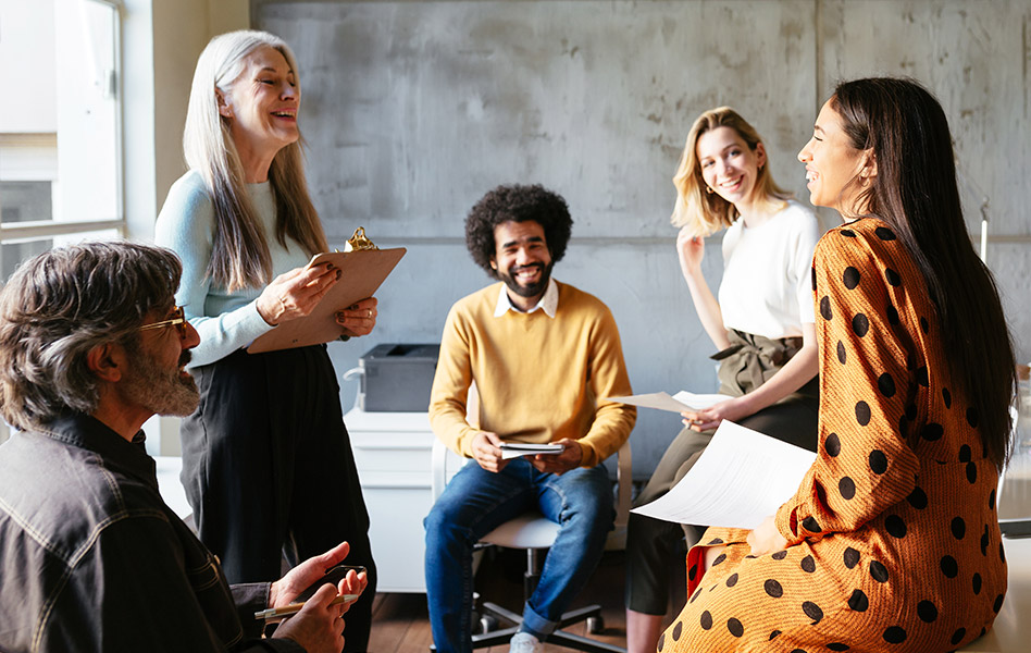 Five coworkers smile as they hold an informal meeting