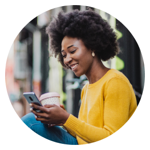A woman in a yellow sweater drinks coffee while checking her phone.
