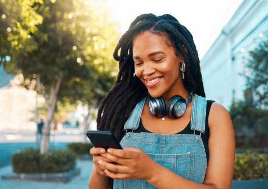 A smiling woman in a city looks at her phone.