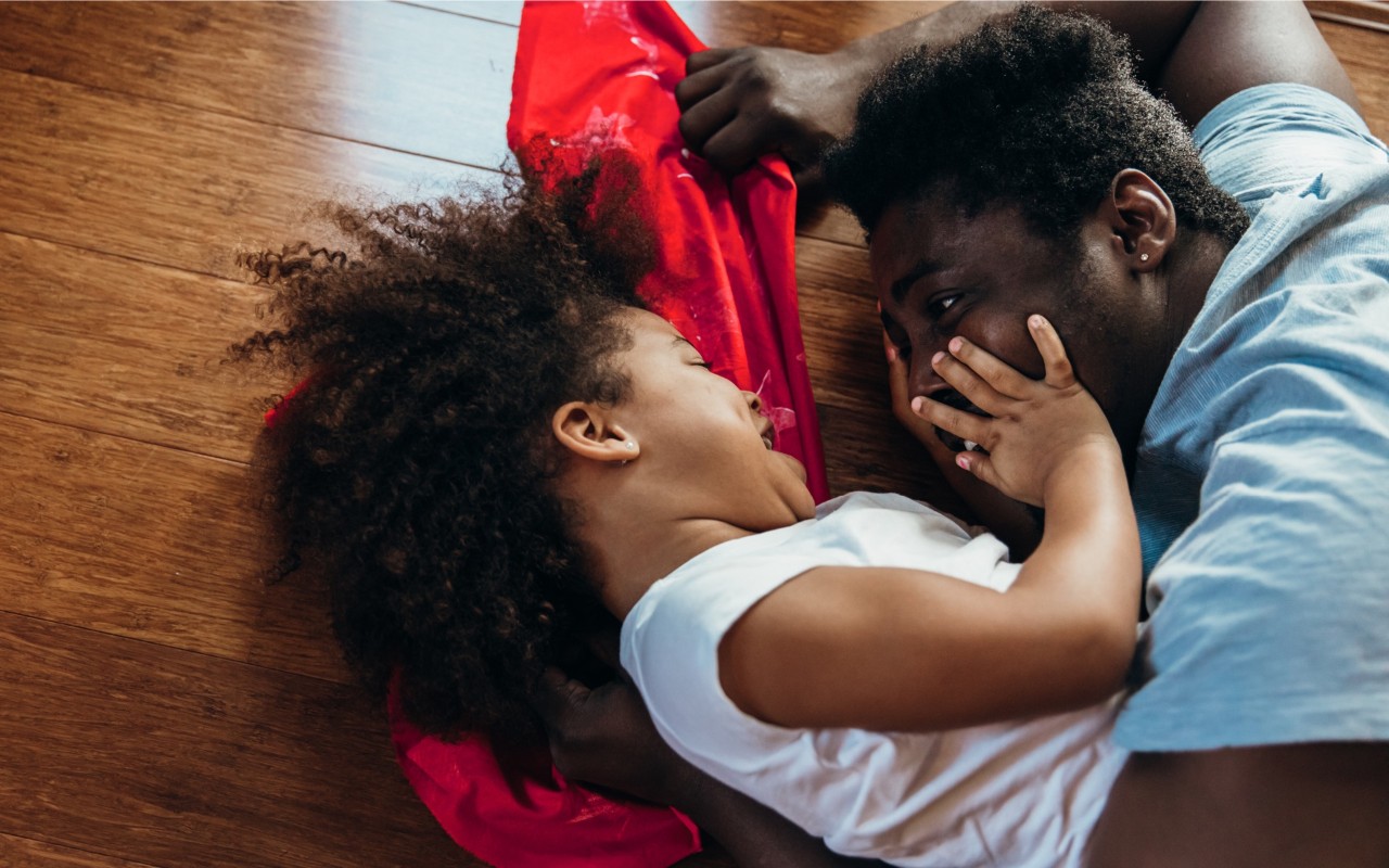Father and young daughter playing on a hardwood floor.