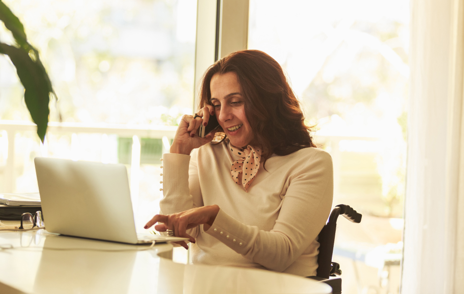 Person in wheelchair working on a laptop while making a phone call. with a smartphone.
