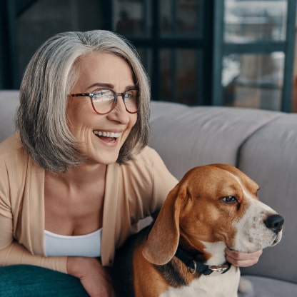 Person sitting on a couch smiling looking out of frame with their arm around a dog.