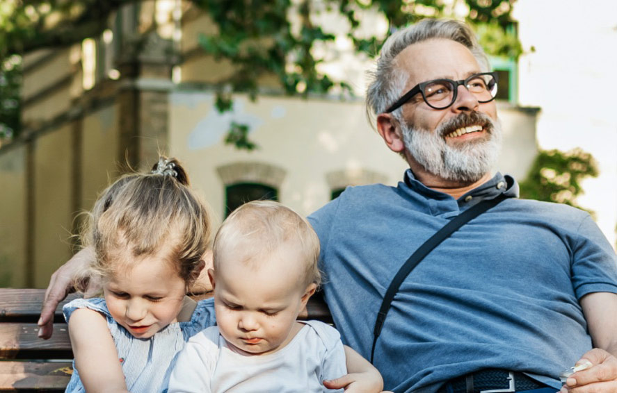 Grandparent smiles contently while sitting with their grandchildren on a park bench.