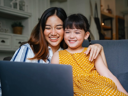 A woman and her daughter are smiling at their laptop during a wealth management family meeting.
