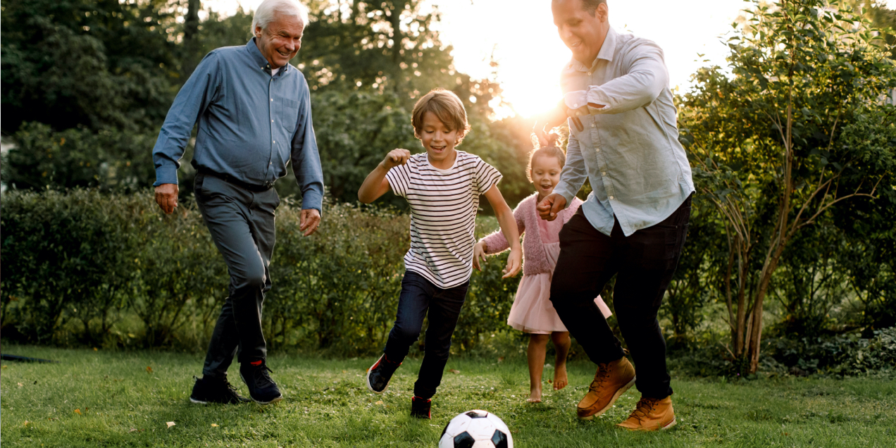 Grandparent, parent, and two children joyfully play soccer outdoors.