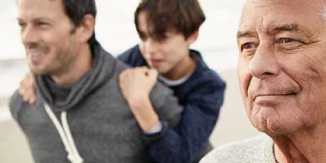 Parent holds child up, while standing next to grandparent, optimistically looking at the horizon.