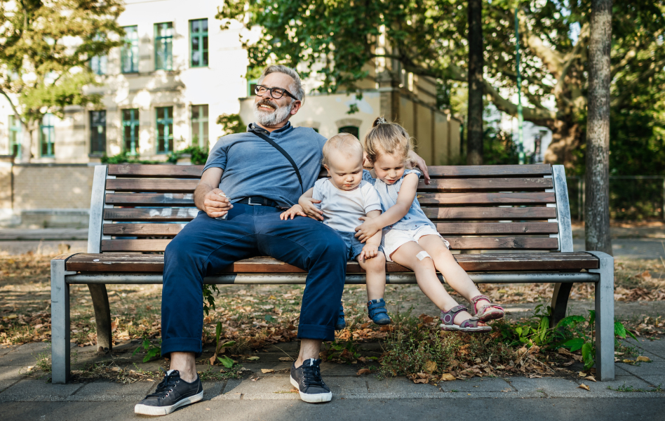 Man sitting on a park bench with his two grandchildren.