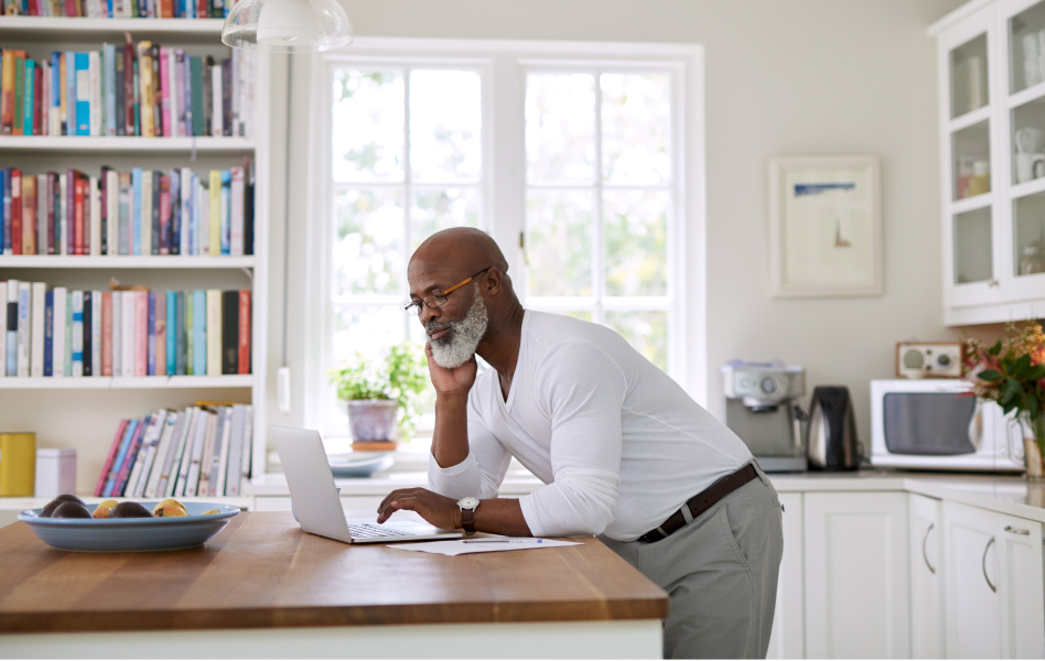 Man uses laptop while standing in his kitchen.