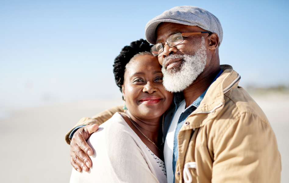 Older couple embrace while walking on the beach.