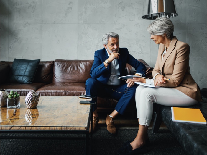 A man and woman sit on sofas while discussing financial matters.