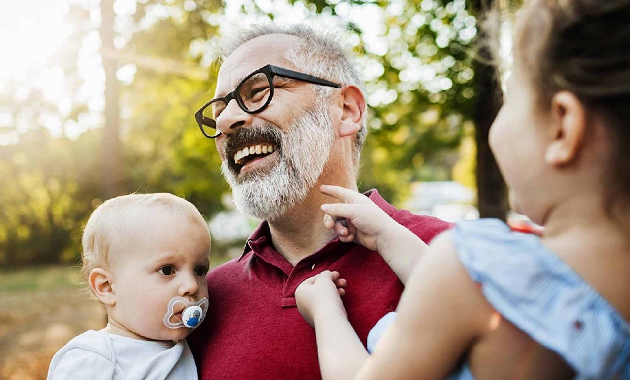 A gentleman holding his grandkids and smiling.